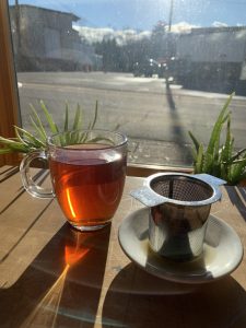 Glass tea mug with burnt-orange liquid inside beside a coaster with a tea strainer on top.